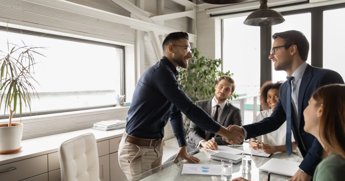 Diverse business partners shaking hand in modern boardroom after negotiation, signing contract, making successful deal, Arabian executive greeting new employee at meeting, group negotiations